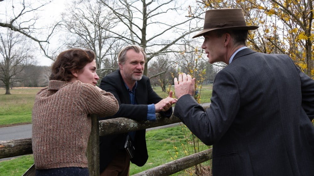 L to R: Emily Blunt (as Kitty Oppenheimer) with writer, director, and producer Christopher Nolan and Cillian Murphy (as J. Robert Oppenheimer) on the set of OPPENHEIMER.